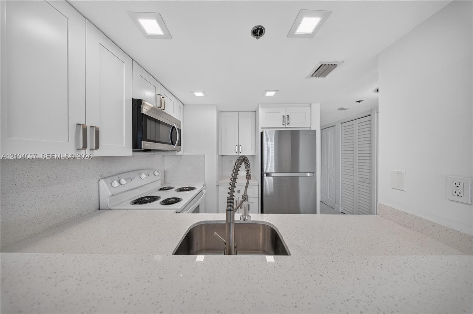 Kitchen featuring white shaker cabinetry, speckled quartz countertops, stainless steel appliances, and a gooseneck faucet