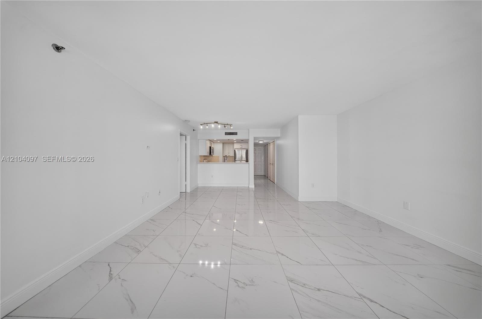 Large-format tile flooring, neutral walls, and a recessed kitchen featuring cabinetry with stainless steel appliances