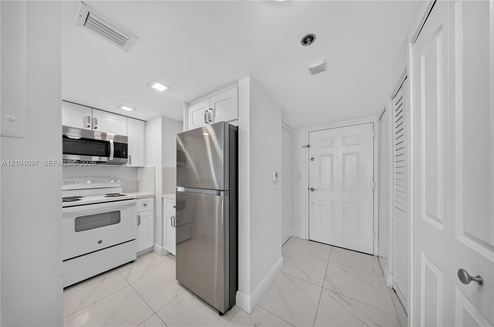 Kitchen featuring white cabinetry, stainless steel refrigerator, white electric range, over-the-range microwave, and large-format tile flooring