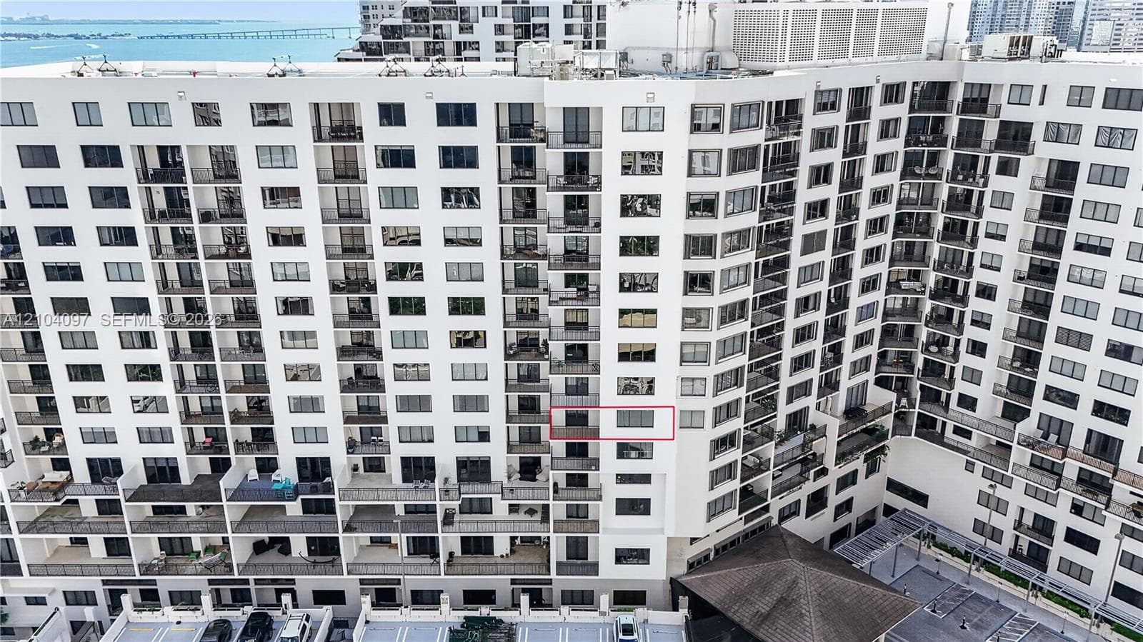 High-rise condominium exterior featuring tiered balconies, white stucco facade, floor-to-ceiling glass doors, and water proximity