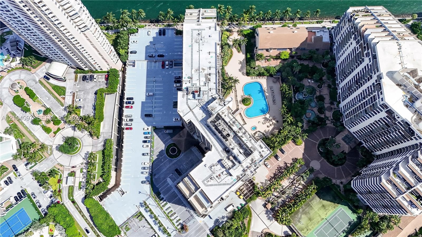 Aerial view featuring a multi-building residential complex, an outdoor swimming pool, paved surface parking, and tennis courts
