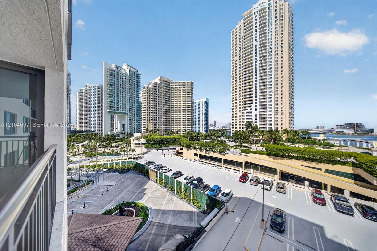 Balcony featuring a metal railing with outdoor scenery including a multi-level parking structure, landscaped grounds, and metropolitan high-rise buildings