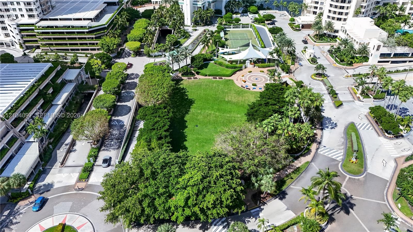 Aerial perspective of the community grounds featuring a central expansive lawn, mature landscaping, paved pathways, and a tennis court