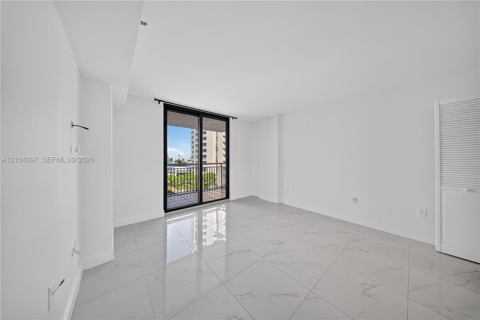 Interior space featuring oversized light-toned tile flooring, large sliding glass doors, a private balcony with metal railing, and louvered-style closet doors