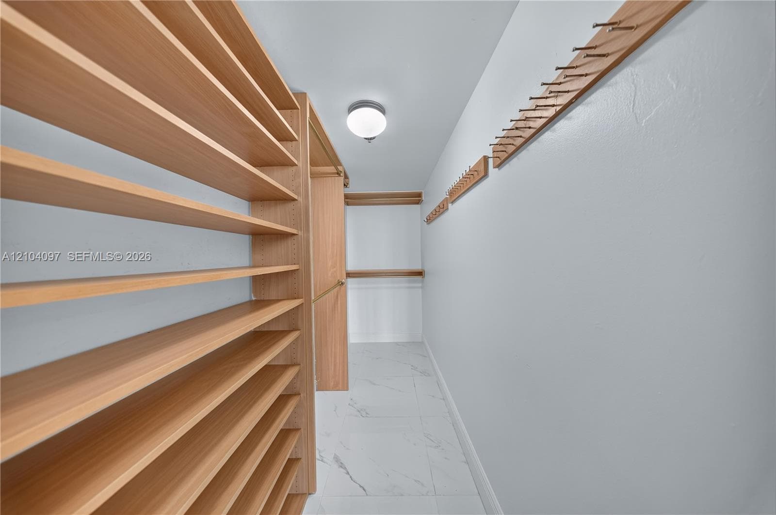 Custom storage space featuring extensive wood-finish shelving, wall-mounted hanging racks, and large-format tile flooring