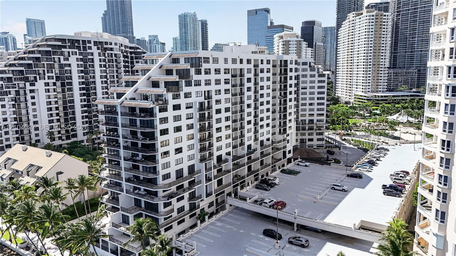 Multi-story residential building featuring private recessed balconies, a structured parking area, and manicured palm landscaping