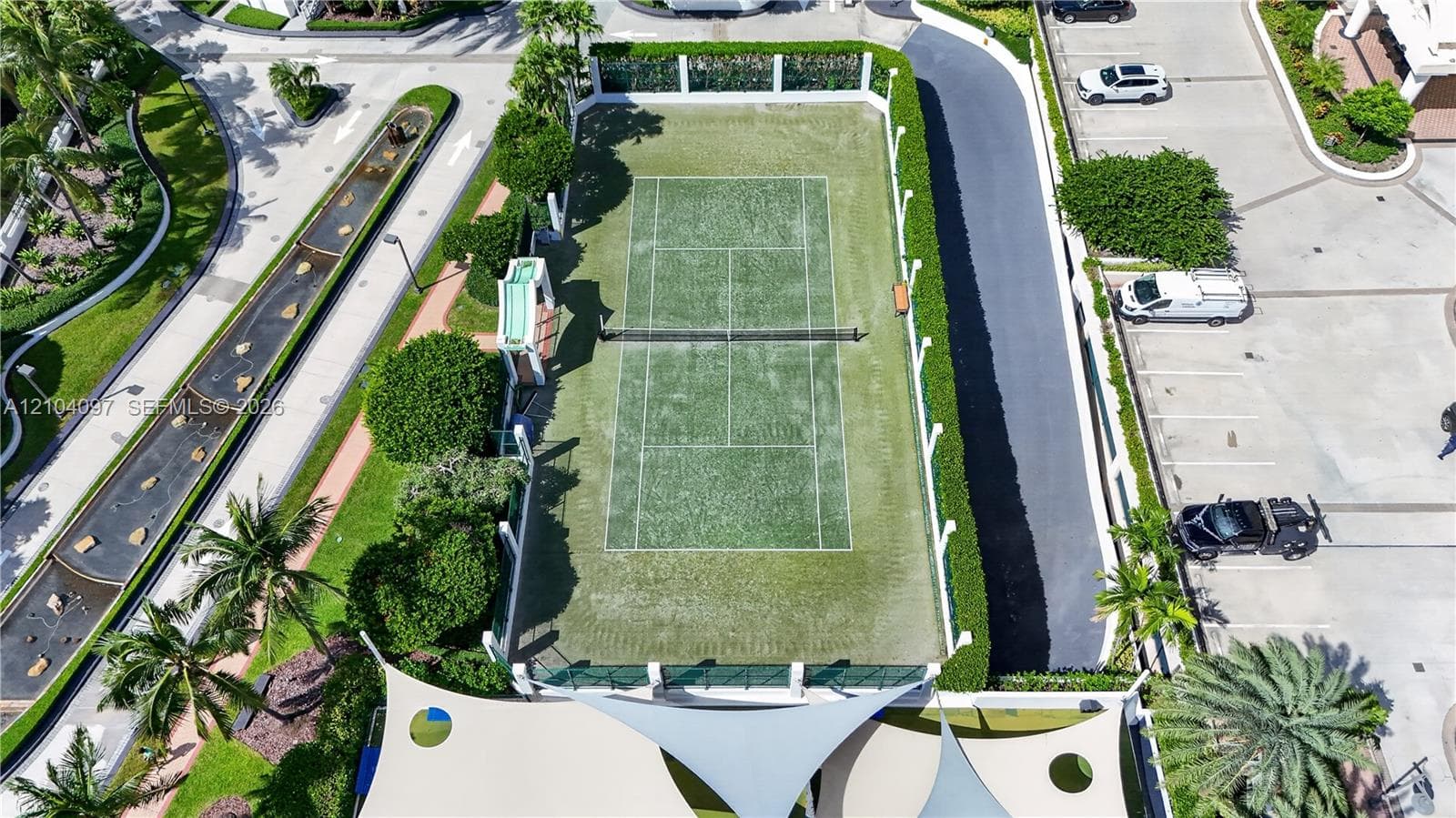 Tennis court featuring a synthetic turf surface, perimeter fencing, and manicured hedge screening