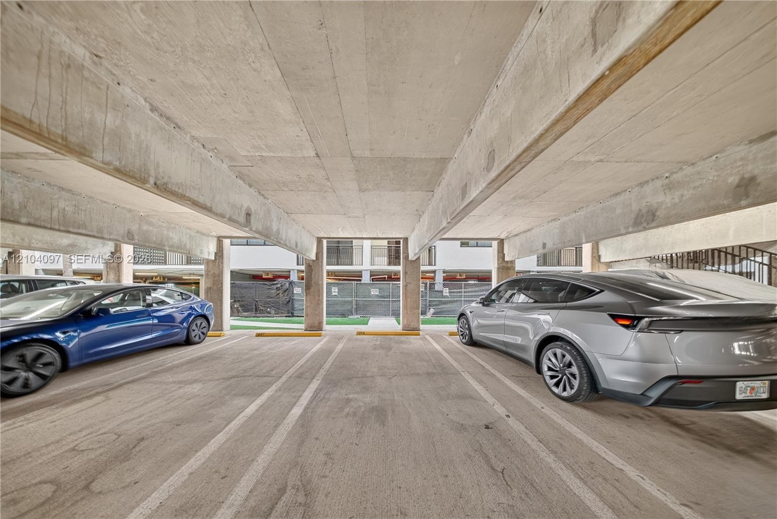 Covered parking garage featuring structural concrete beams, concrete flooring, and designated stalls