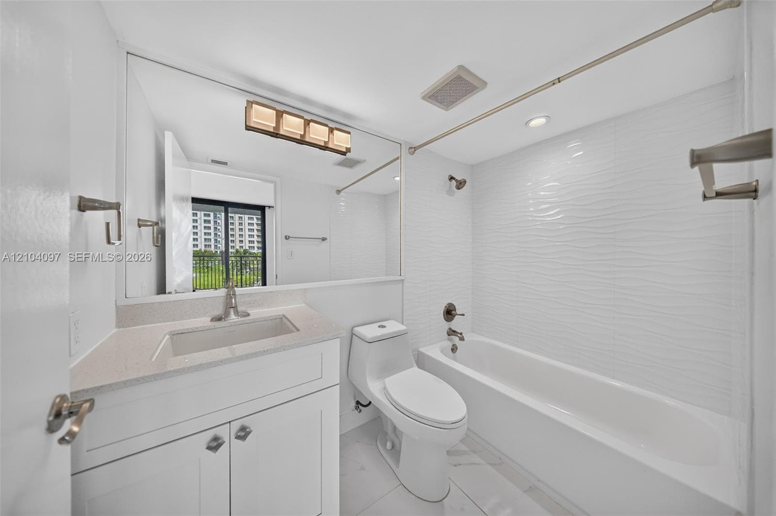 Bathroom featuring a vanity with a stone-composite countertop, full-width mirror, tile flooring, and a tub with a textured tile surround