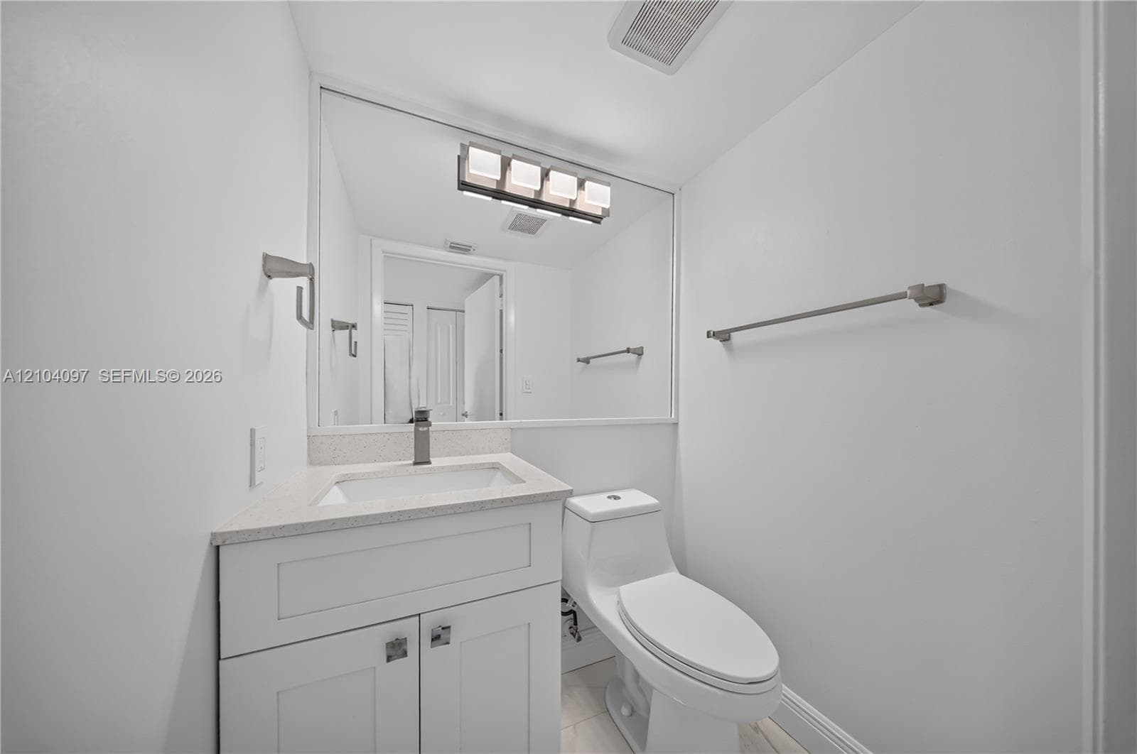 Bathroom featuring white cabinetry, stone-finish countertop, single-basin integrated sink, chrome-finish faucet, and a wall-mounted four-light fixture