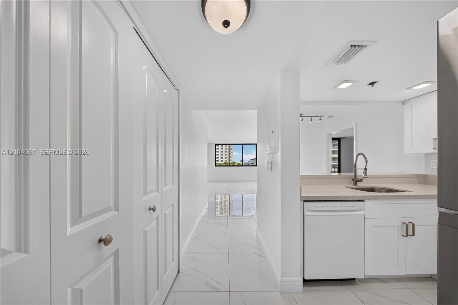White shaker-style cabinetry, neutral stone-finish countertops, stainless steel undermount sink with arched pull-down faucet, porcelain tile flooring, and floor-to-ceiling built-in closet storage