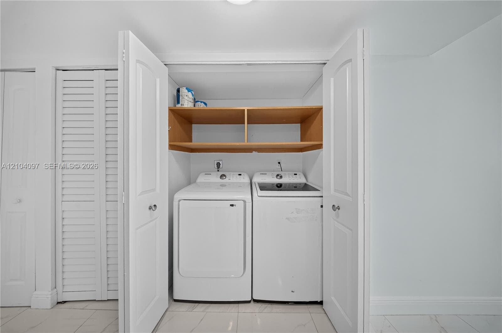 Laundry area featuring wood-finish open shelving, white double-panel doors, and polished stone-finish flooring