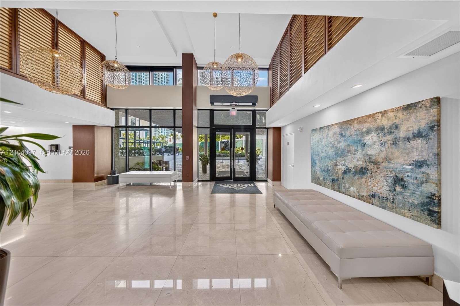 Grand lobby entrance featuring polished stone flooring, double-height ceilings, floor-to-ceiling glass paneling, decorative woven pendant lighting, and slatted wood-finish accent walls