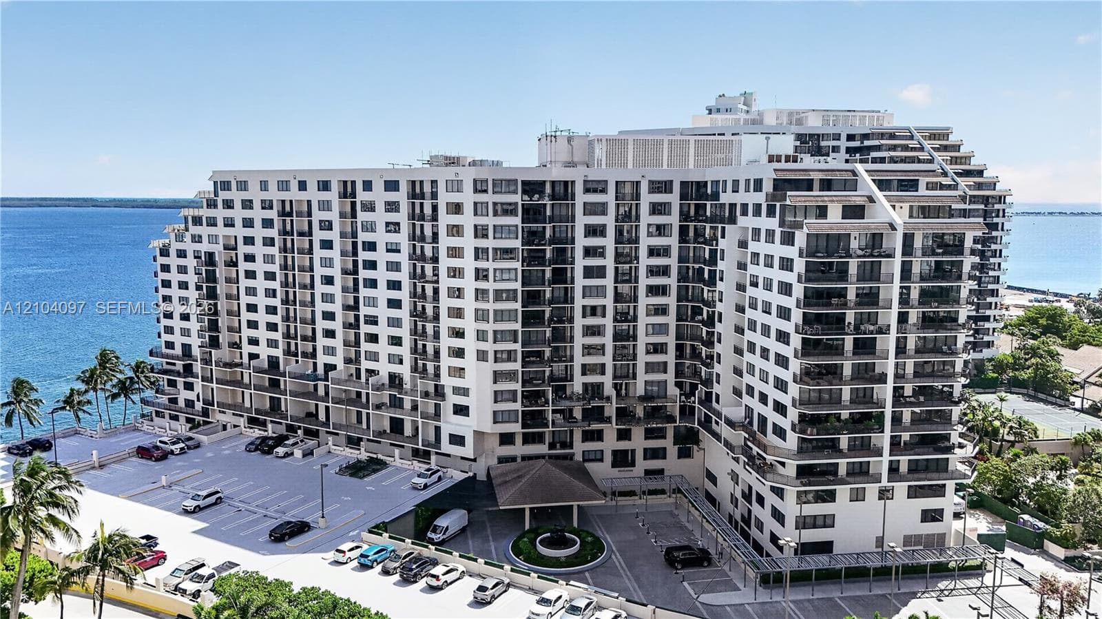 Multi-story high-rise building featuring private balconies, surface parking, paved drive entry, and waterfront positioning