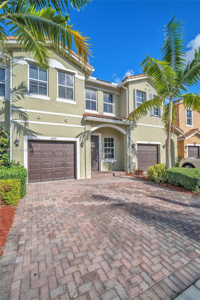 Two-story stucco exterior with dual garage doors, a covered entry, and a paver driveway