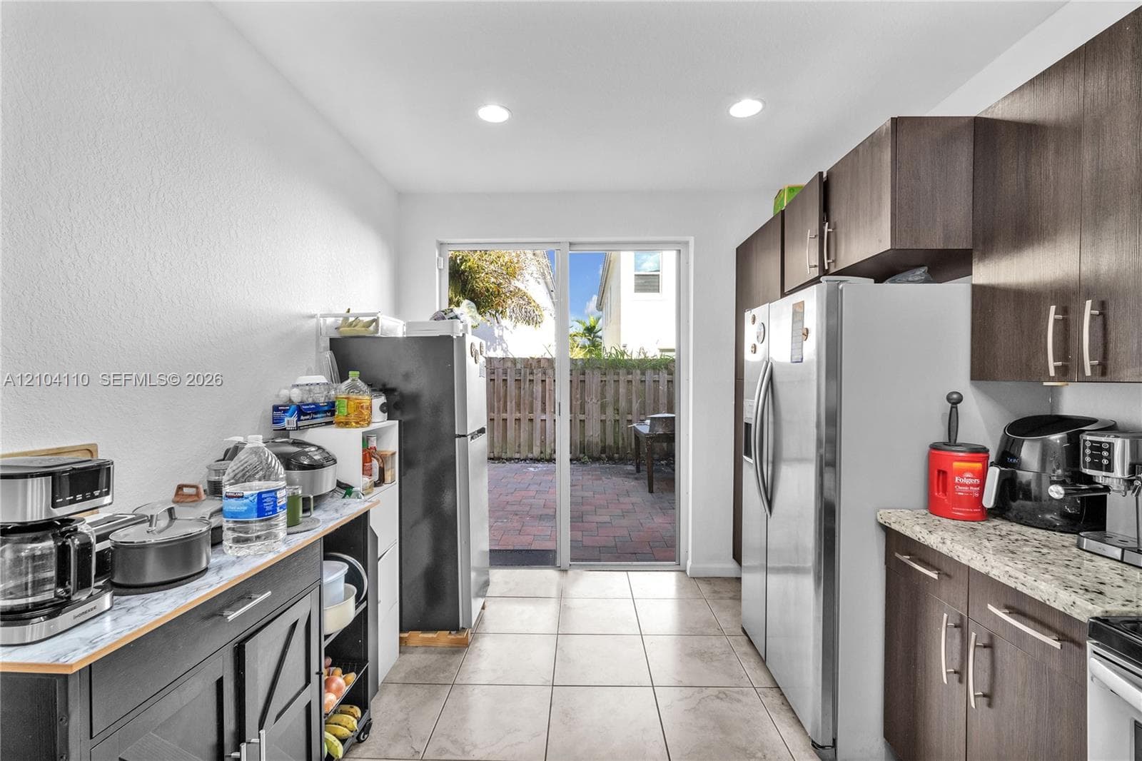 Kitchen with tile flooring, recessed lighting, wood-finish cabinetry, and a sliding glass door to a paved patio