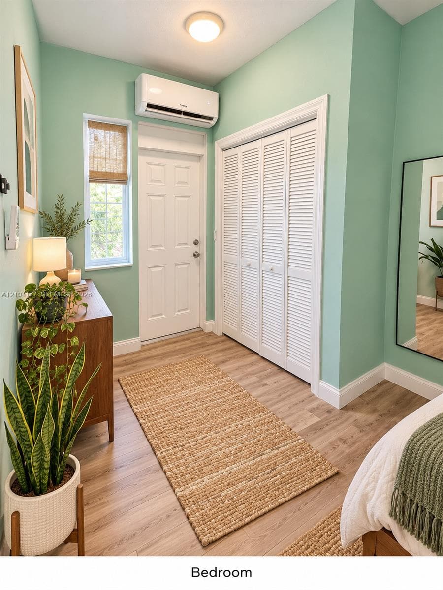 Wood-finish flooring, white louvered closet doors, wall-mounted ductless air conditioning unit, single-hung window with a woven shade, and flush-mount ceiling lighting