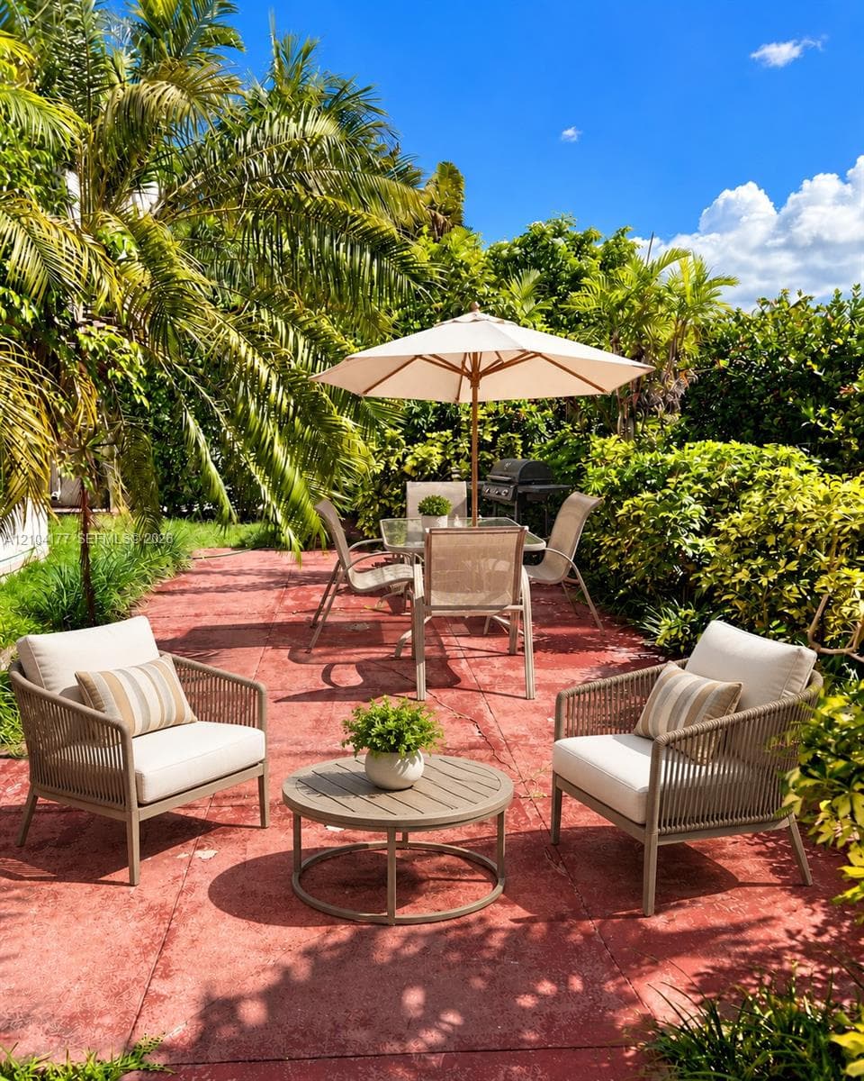 Outdoor patio featuring square concrete paving, lush perimeter landscaping, and mature palm trees