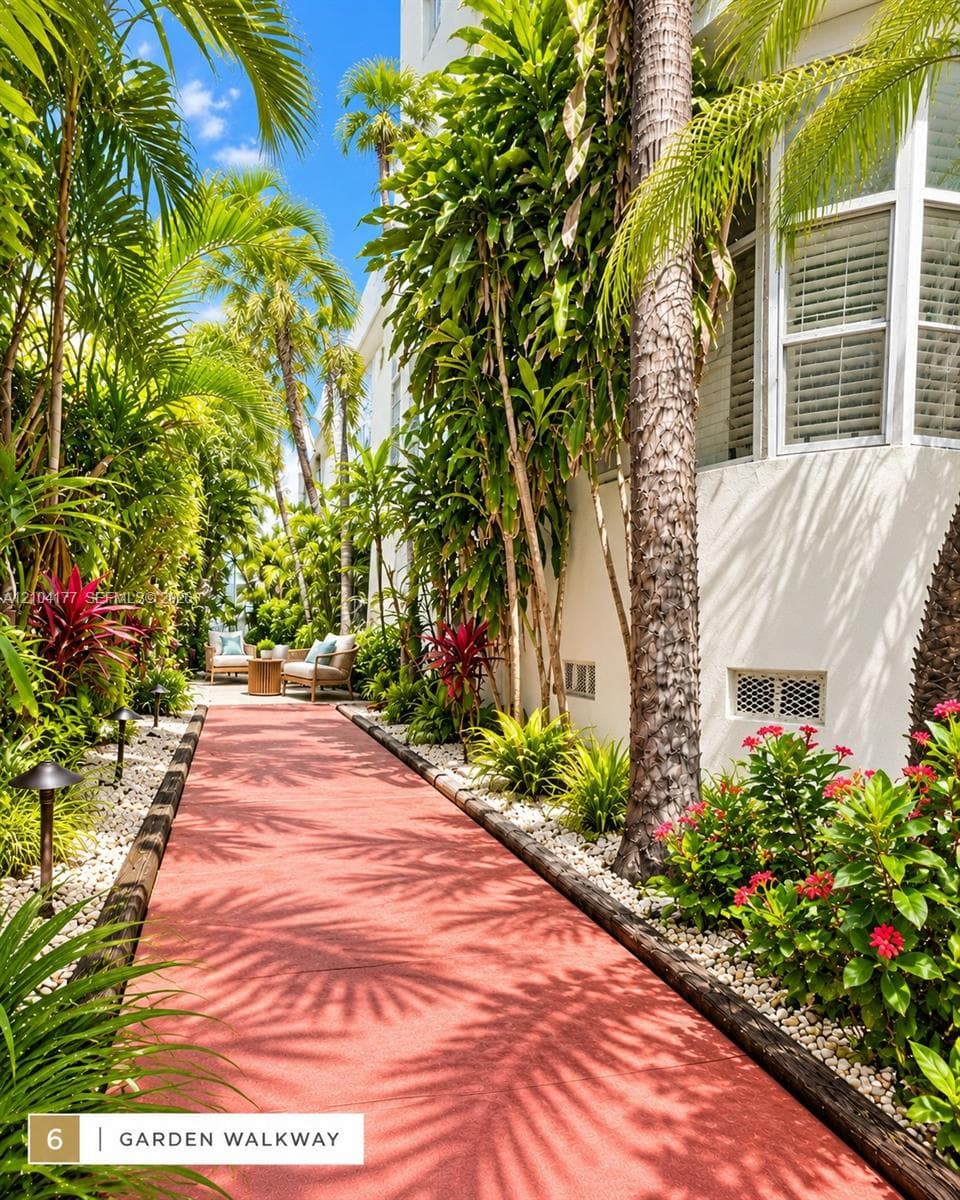 Red paver garden walkway bordered by timber edging, white stone landscaping, lush tropical foliage, and low-voltage path lighting
