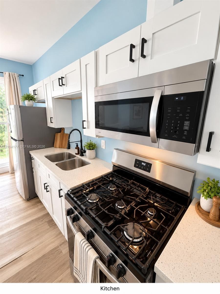 Kitchen featuring white shaker-style cabinetry with matte black hardware, stainless steel gas range and microwave, light-toned stone-finish countertops, and wood-finish flooring