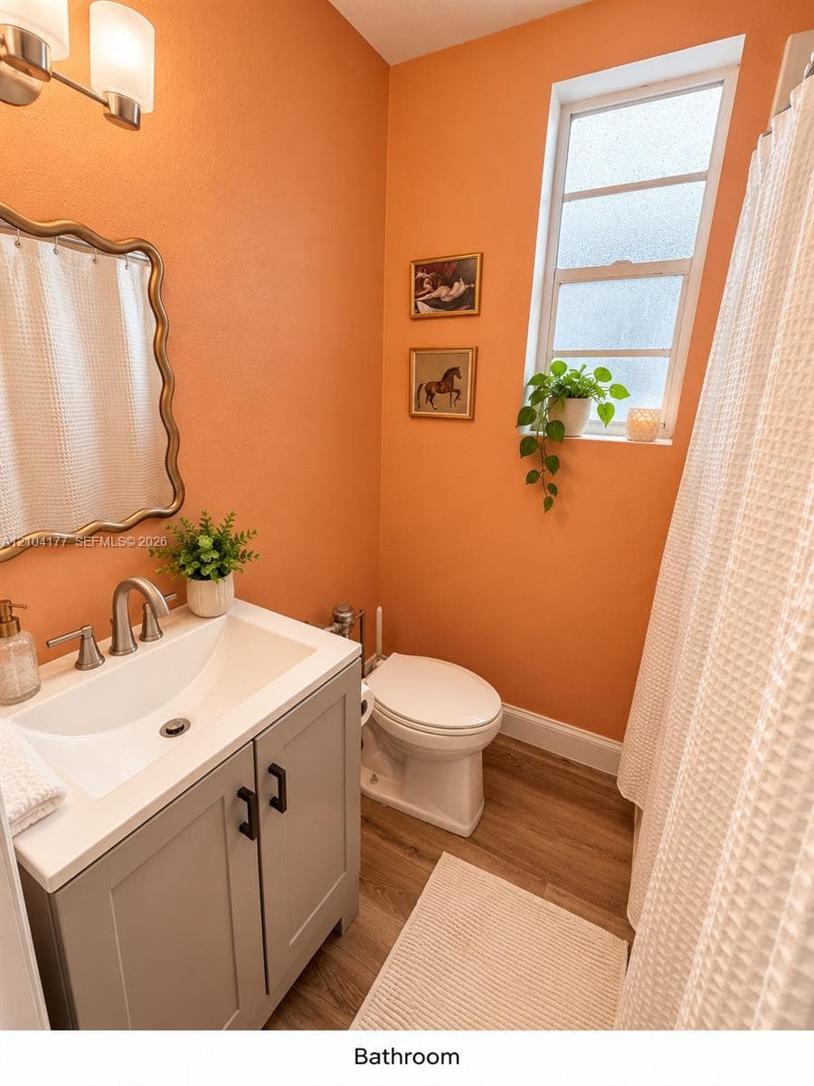 Bathroom featuring a vanity with a white composite countertop, an undermount sink with a metallic faucet, wood-finish flooring, a wall-mounted light fixture, and a vertical window with obscured glass