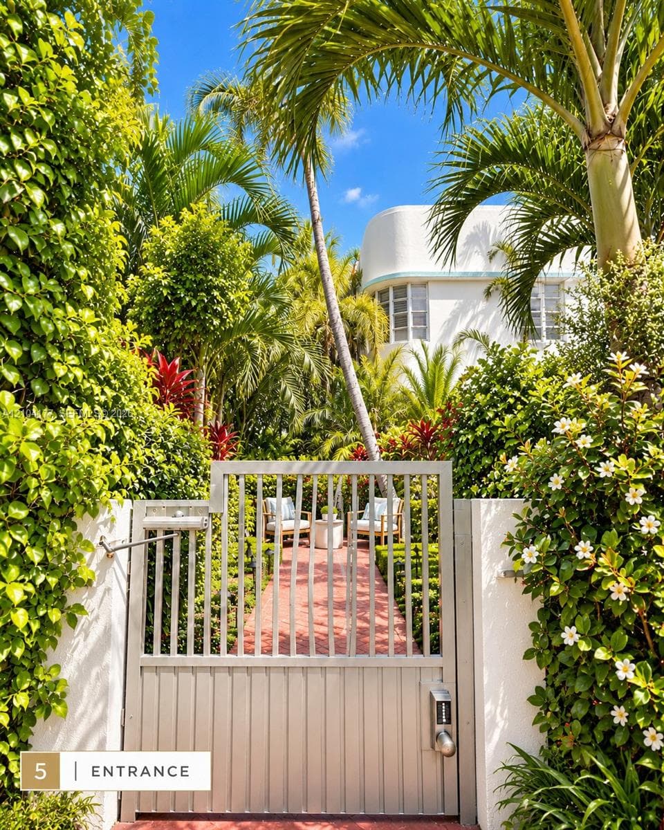 Streamlined metal pedestrian gate with integrated electronic keypad entry, finished brick pathway, and lush perimeter landscaping featuring mature palm trees