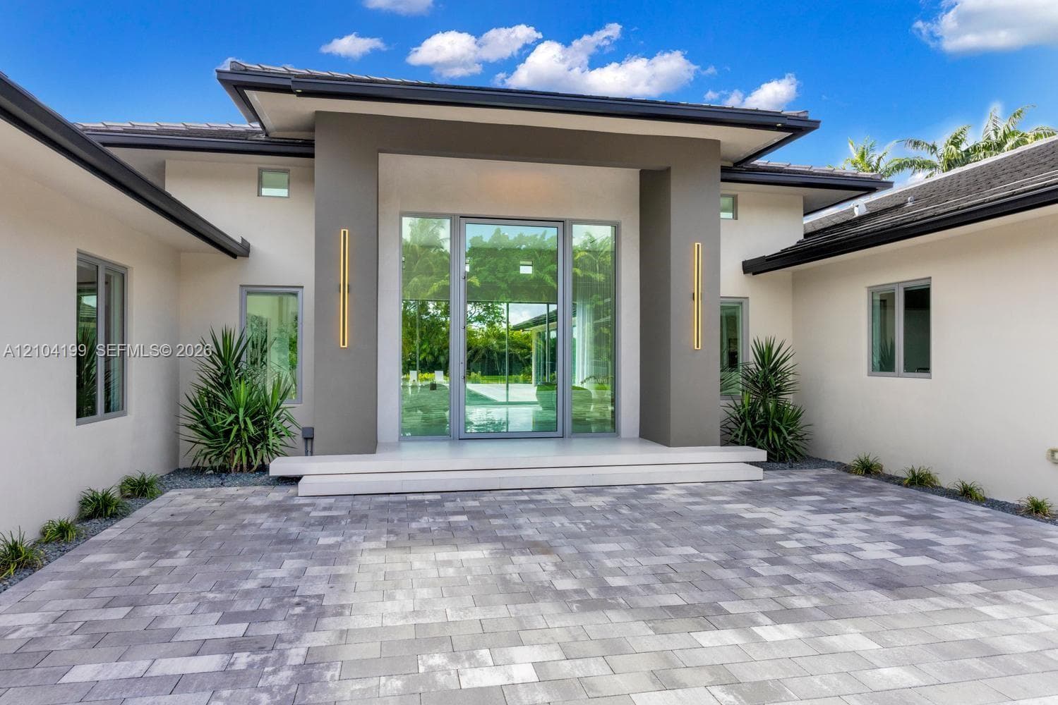 Outdoor living area featuring stone paver decking, an in-ground infinity-edge pool, a raised spa, and floor-to-ceiling glass sliding doors