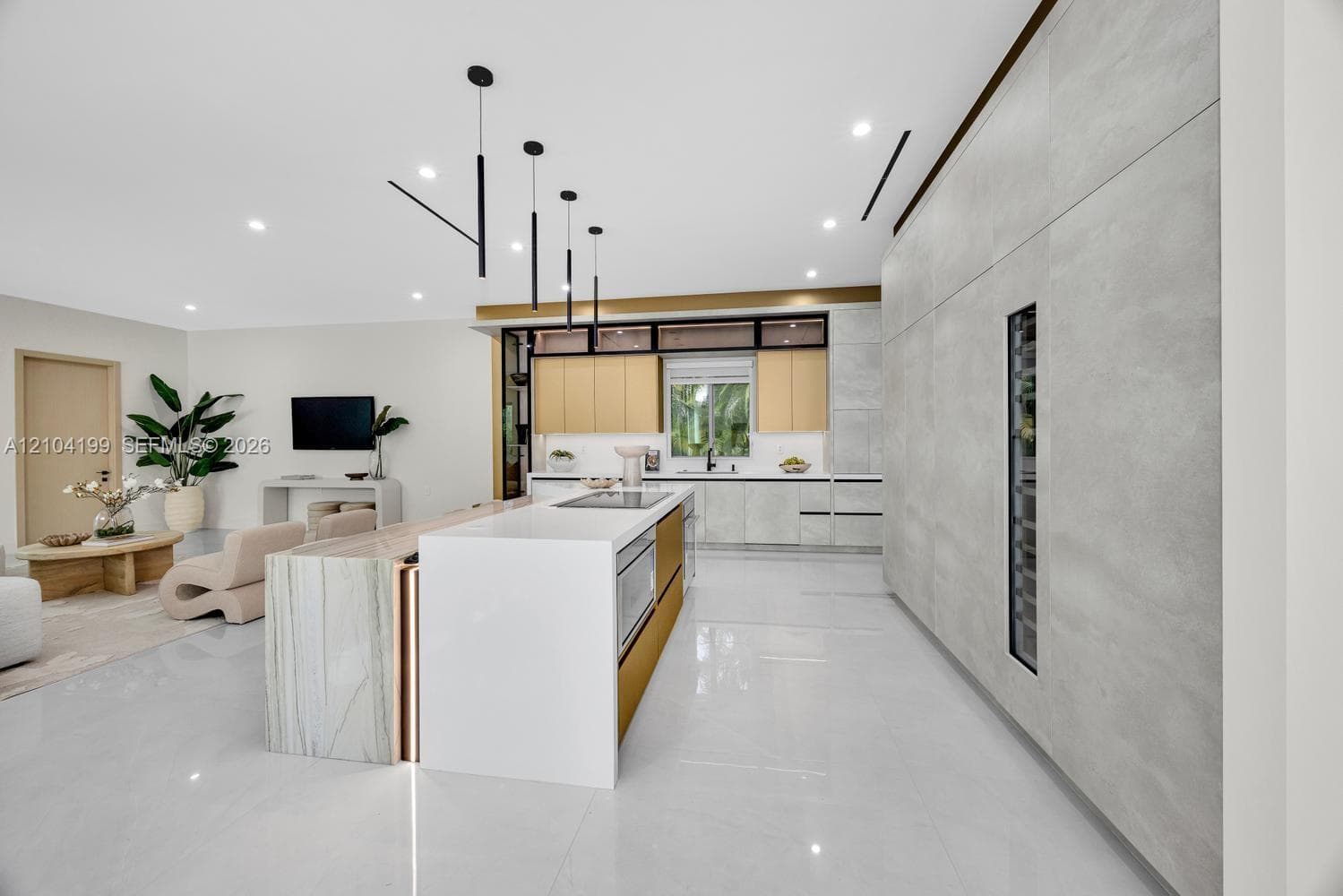 Modern kitchen featuring a central island with integrated cooktop and oven, sleek flat-panel cabinetry, light-toned stone-surface countertops, recessed ceiling lighting, and minimalist linear pendant fixtures