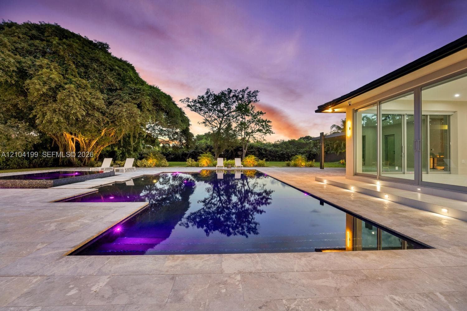Contemporary exterior featuring floor-to-ceiling sliding glass doors, integrated ground-level accent lighting, stone-tiled patio, and a recessed swimming pool