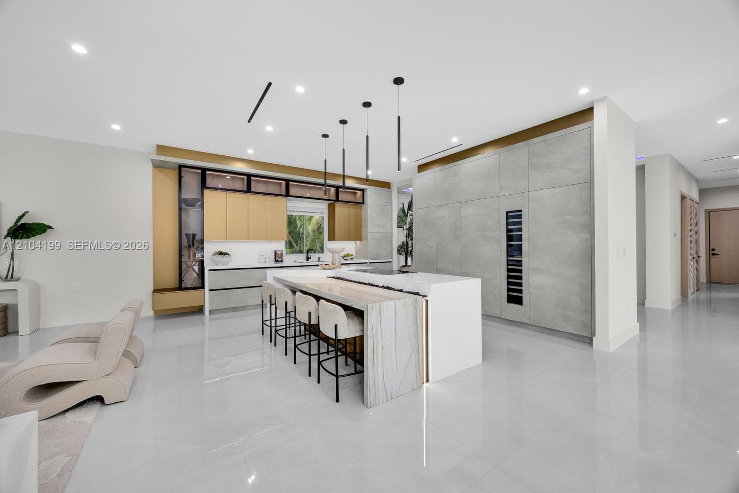 Kitchen featuring a central island with waterfall-edge countertop, floor-to-ceiling cabinetry with integrated beverage storage, matte metallic base accents, and linear pendant lighting