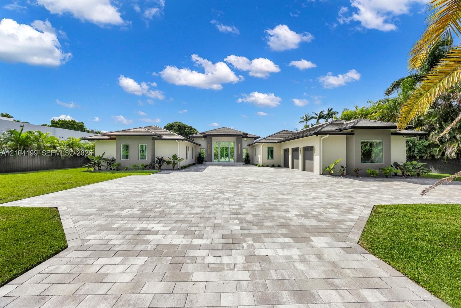 Modern architectural exterior featuring a paved stone driveway, recessed entry with a double-height frame, full-height glass entryway, and vertical wall-mounted lighting