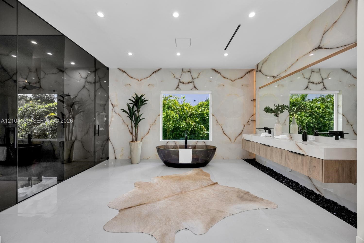 Bathroom featuring floor-to-ceiling stone wall cladding, a freestanding oval soaking tub, a smoked-glass enclosed shower, a floating vanity with stone surfacing, and polished large-format tile flooring