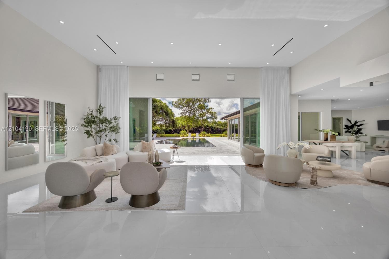 Expansive open-concept room featuring high ceilings with recessed lighting, large-format polished tile flooring, and floor-to-ceiling glass sliding doors
