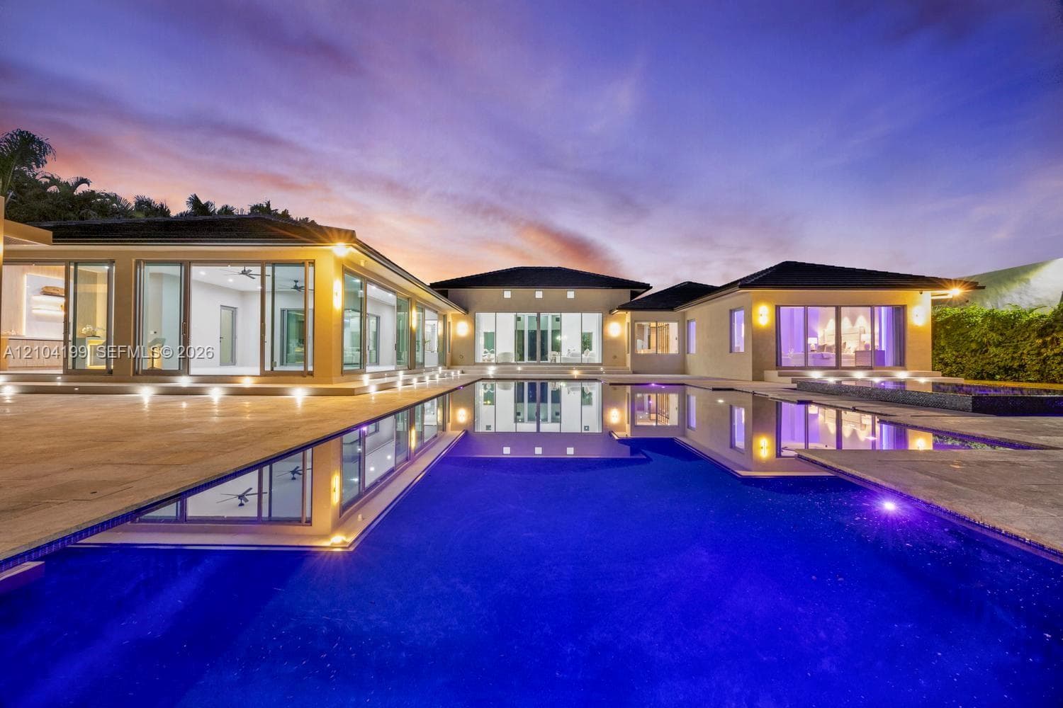 Modern exterior entrance featuring a glass-panel pivoting entry door, dual elevated concrete steps with integrated lighting, sleek vertical wall sconces, and stone paver driveway