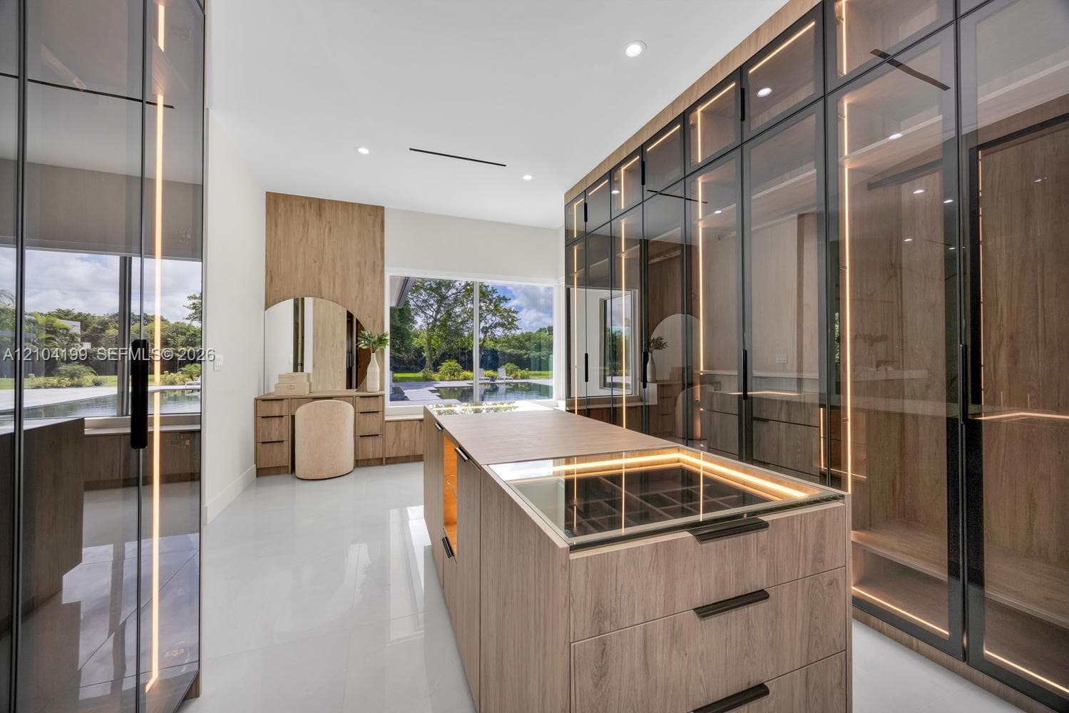Floating grey vanity with integrated double sinks, oversized organic-shaped wall mirror with backlighting, wood-finish wall paneling, and glass-enclosed shower with tiled surround