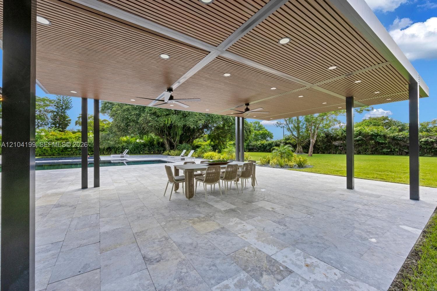 Gated entrance featuring a wide paver driveway, concrete pillar accents, vertical metal fencing, and mature palm landscaping