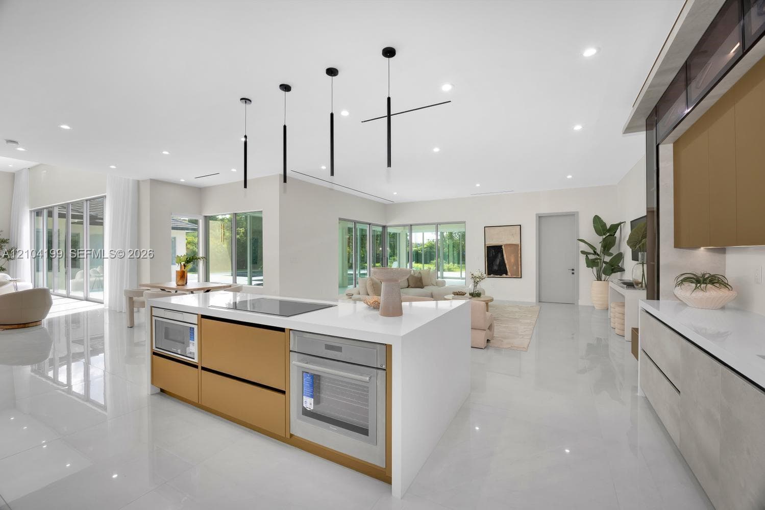 Open-concept living space featuring large-format tile flooring, recessed linear lighting, sliding glass walls, and custom cabinetry with stone-surfaced waterfall island