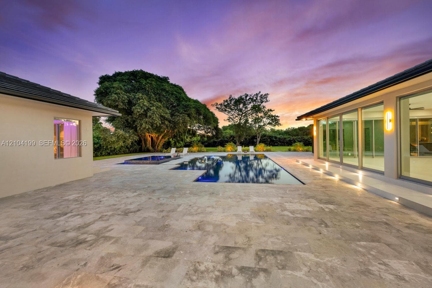 Expansive backyard featuring a manicured lawn, perimeter landscaping, mature trees, a paved patio, and a pergola