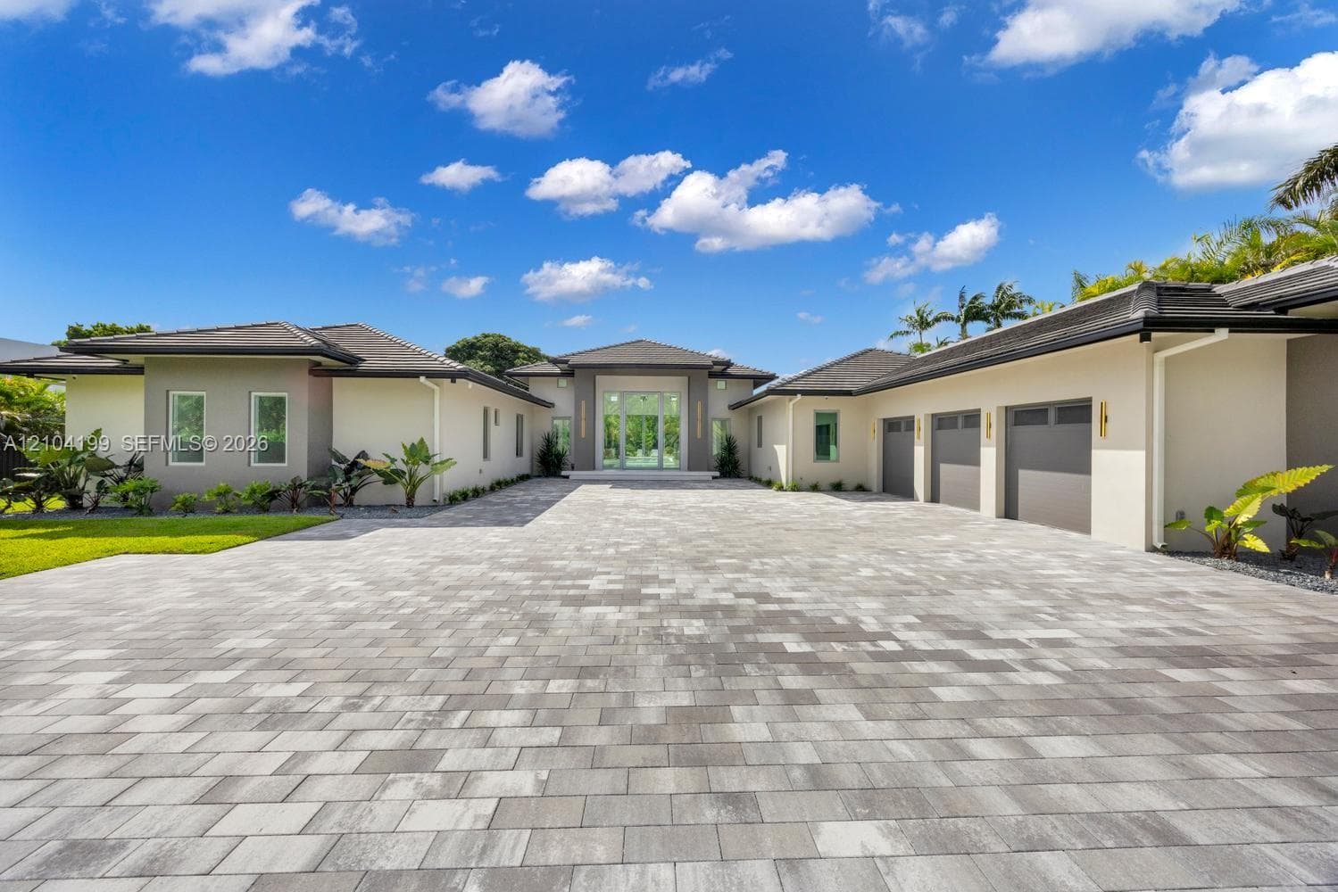 Modern entryway featuring an oversized glass pivot door, dual tiered concrete steps, linear wall-mounted exterior lighting, and a paved stone driveway