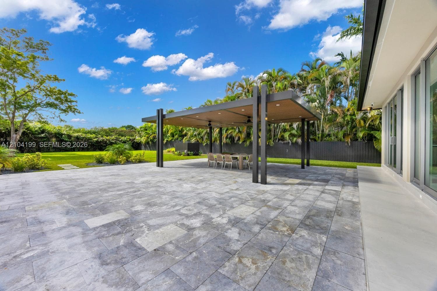 Contemporary single-story exterior featuring a paver stone driveway, multi-car garage, manicured lawn, and full-height glass entryway