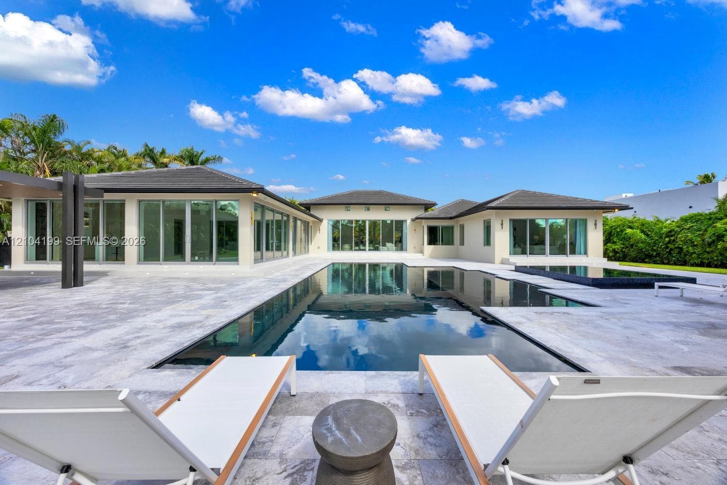 Backyard featuring a custom infinity-edge pool, a raised square spa with tile surfacing, extensive stone paver decking, and a covered pavilion structure