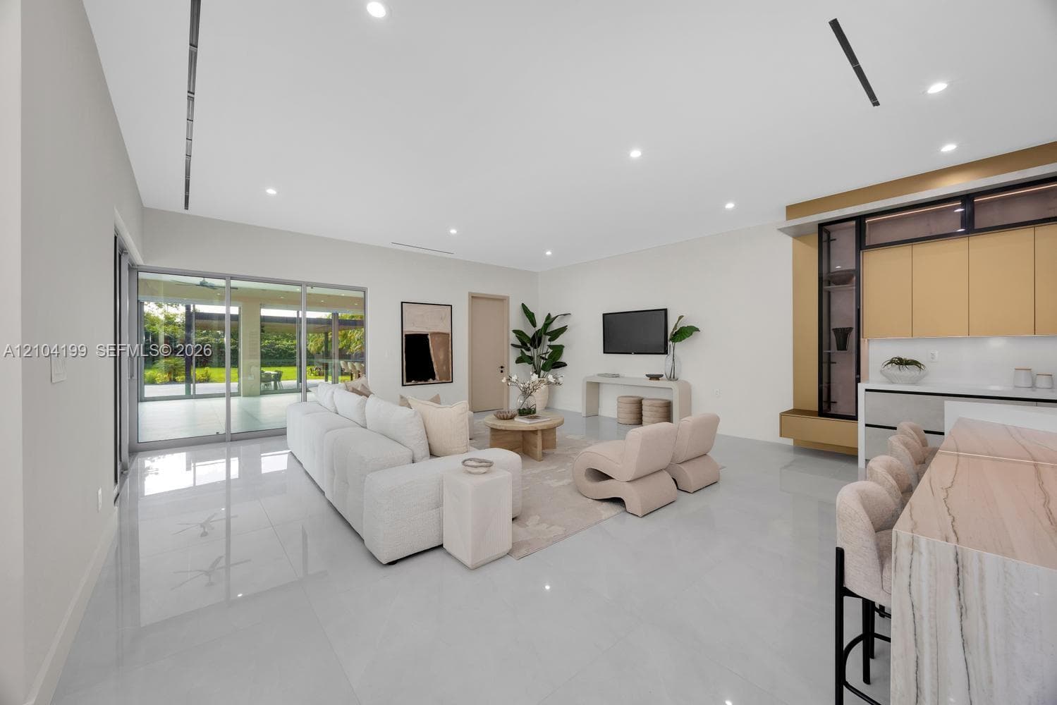Open-concept interior featuring large-format tile flooring, recessed ceiling lighting, a waterfall-edge kitchen island, metallic accent detailing, and multi-panel sliding glass doors