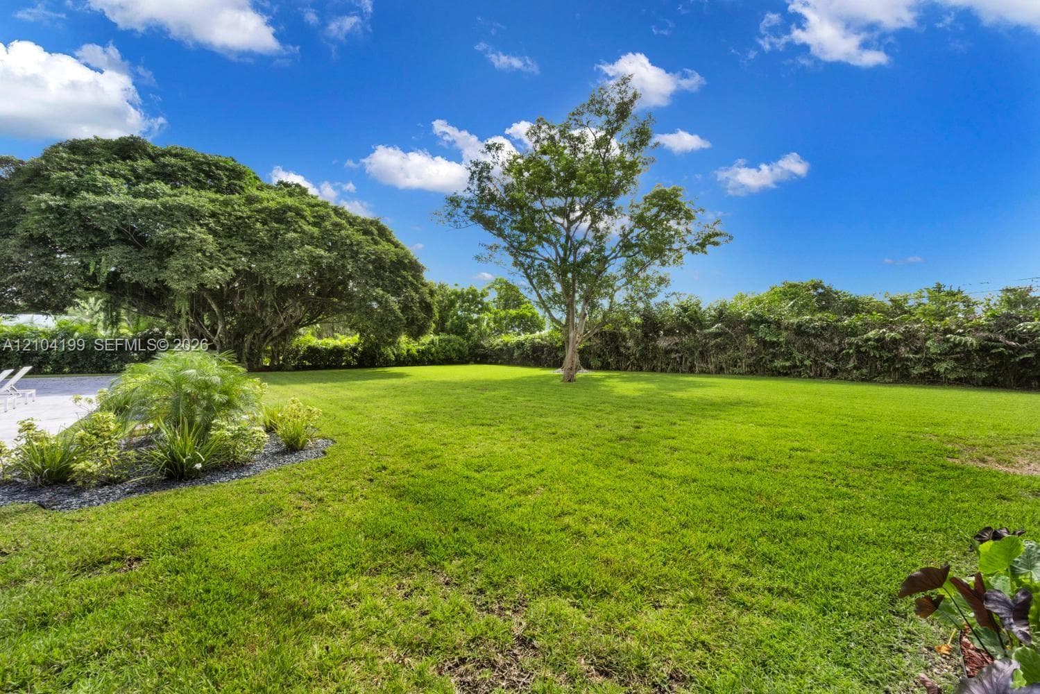 Spacious stone-paved patio featuring a covered pergola with recessed lighting and ceiling fans, manicured lawn, and privacy fencing