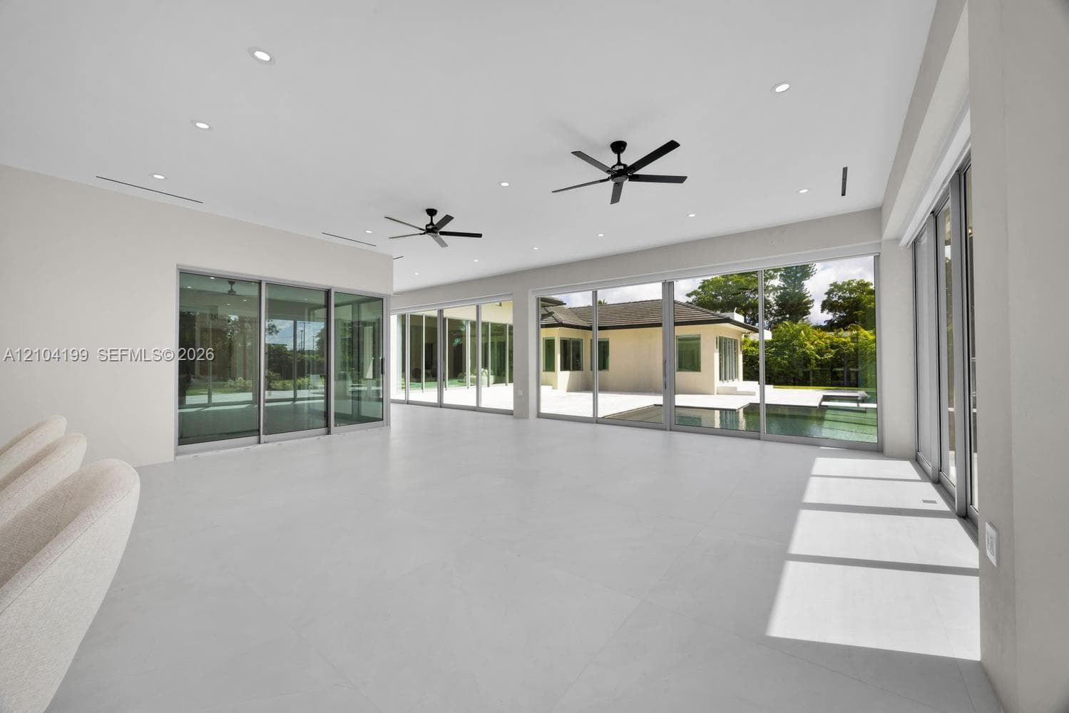Large-format porcelain tile flooring, expansive floor-to-ceiling sliding glass doors, built-in wet bar with wood-panel detailing, recessed lighting, and dual matte black ceiling fans