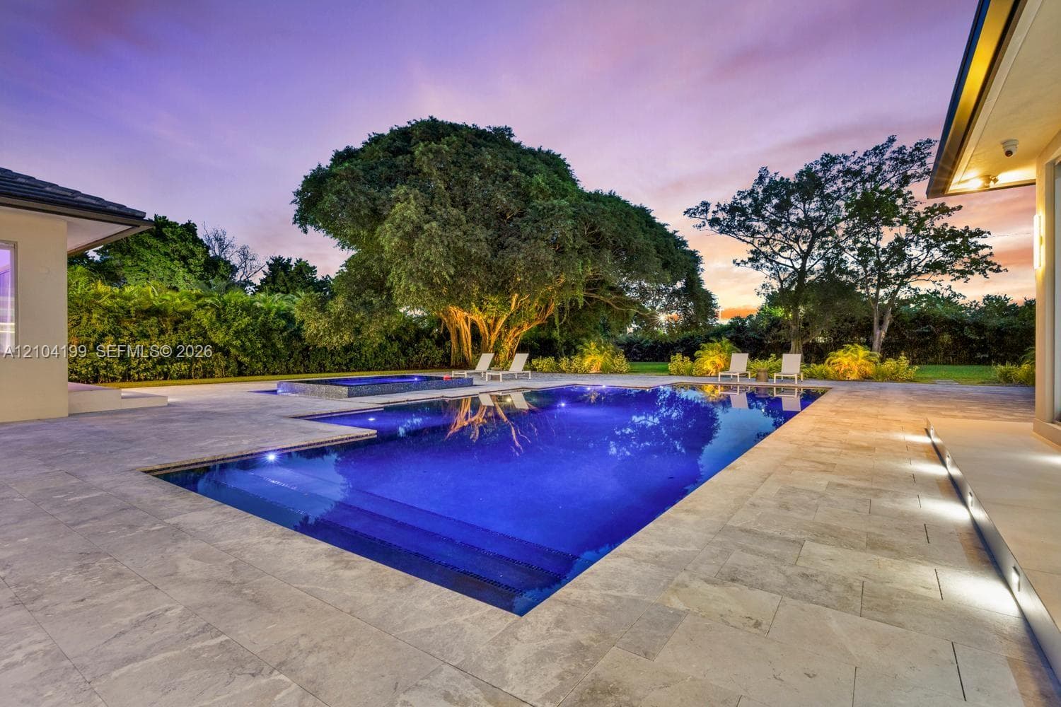 Contemporary residence featuring an infinity-edge pool, stone-paved patio, recessed exterior lighting, and floor-to-ceiling glass sliding doors
