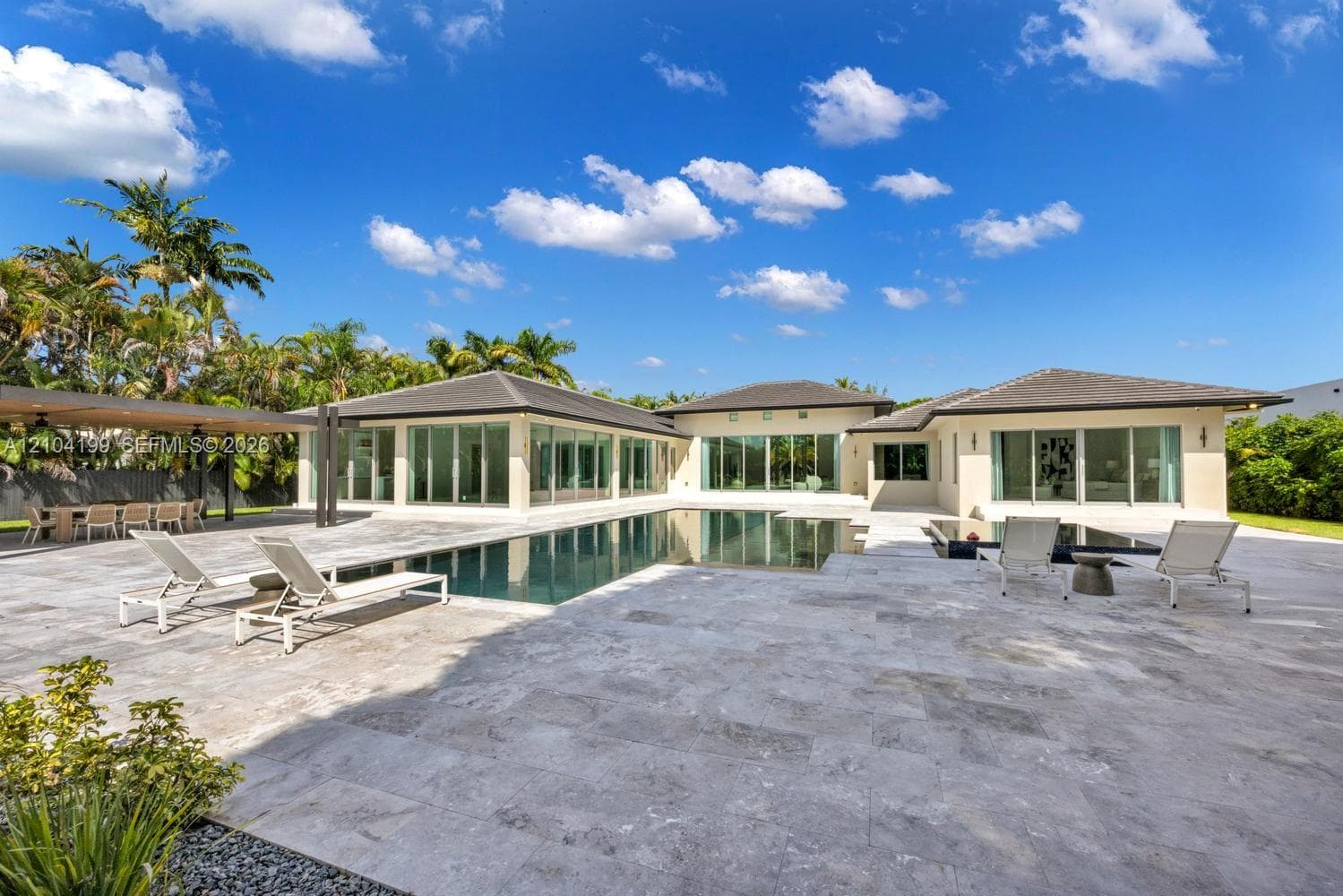 Modern stucco exterior featuring a tiered roofline, expansive paver courtyard, floor-to-ceiling glass entryway, and wall-mounted linear lighting