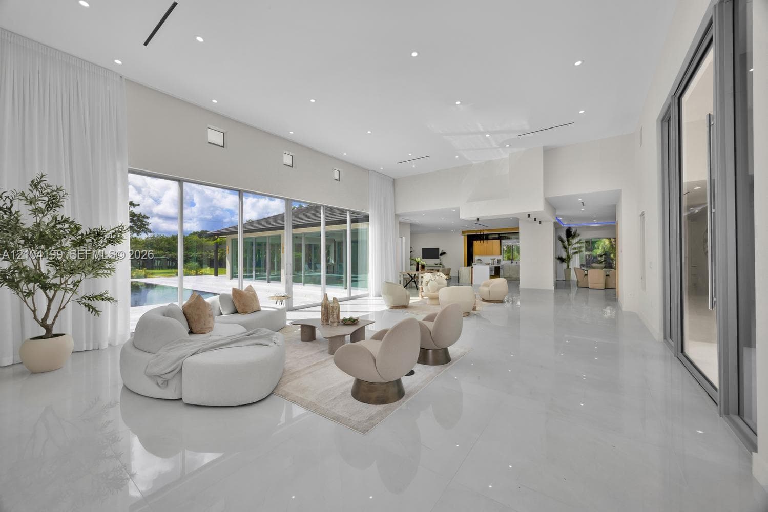 Open-concept living space featuring high-gloss tile flooring, recessed lighting, a tiered tray ceiling with cylindrical pendant fixtures, and floor-to-ceiling glass panel walls