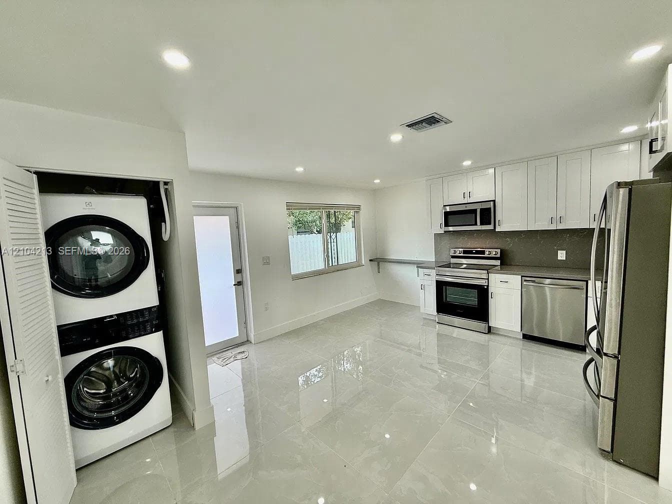 Modern kitchen featuring white shaker cabinetry, stainless steel appliances, and a gray backsplash