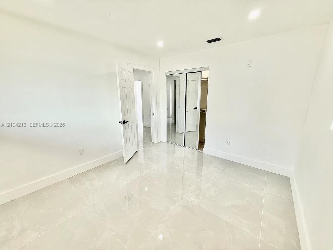 Spacious room featuring light-toned tile flooring, white walls, a recessed light fixture, and a mirrored closet