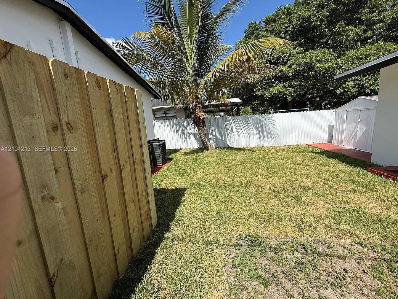 Fenced yard featuring a wooden privacy fence, a white perimeter fence, a mature palm tree, and a grass lawn
